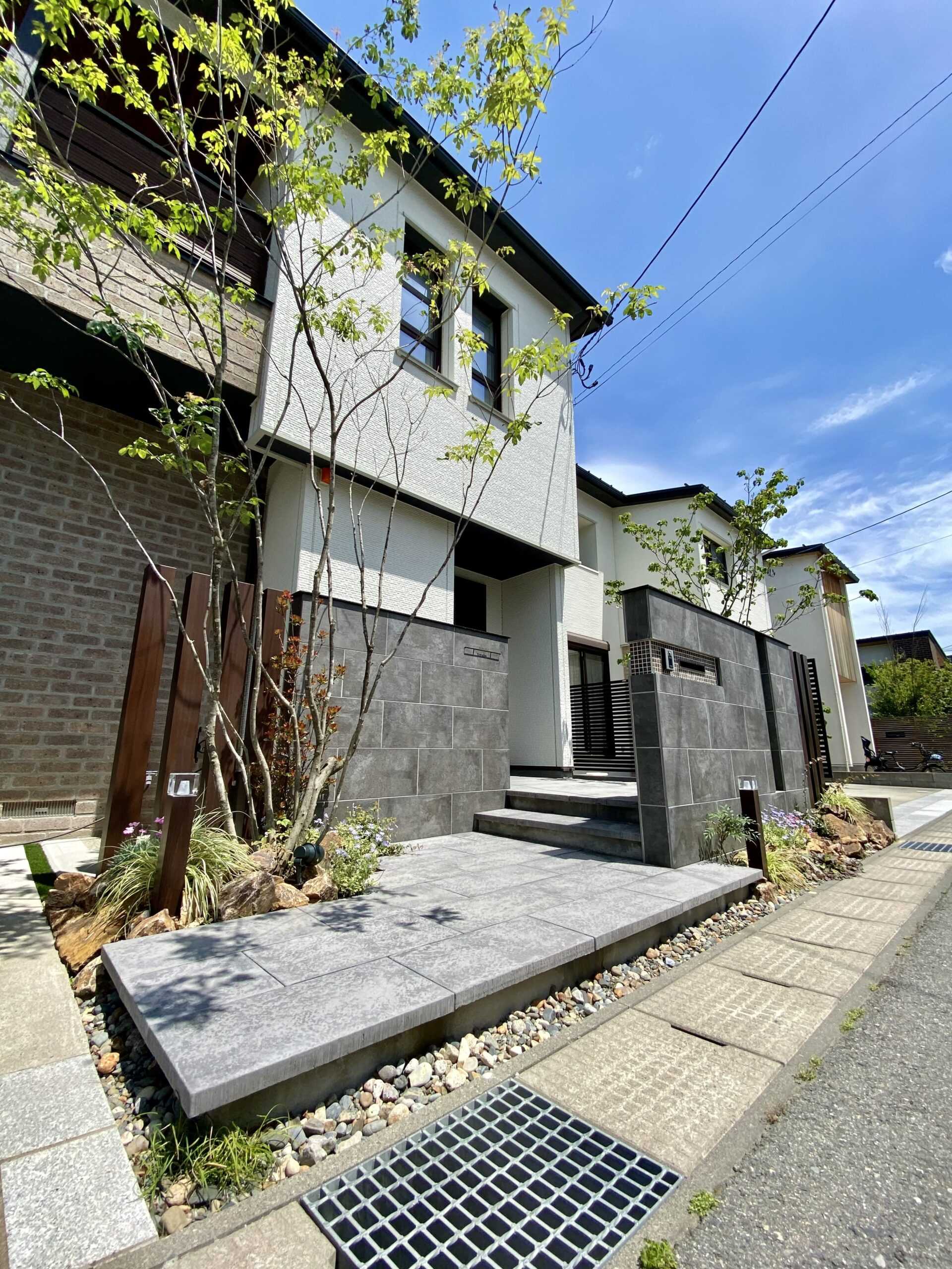 植栽で彩られた、自然石風の舗装材を用いたアプローチと門袖