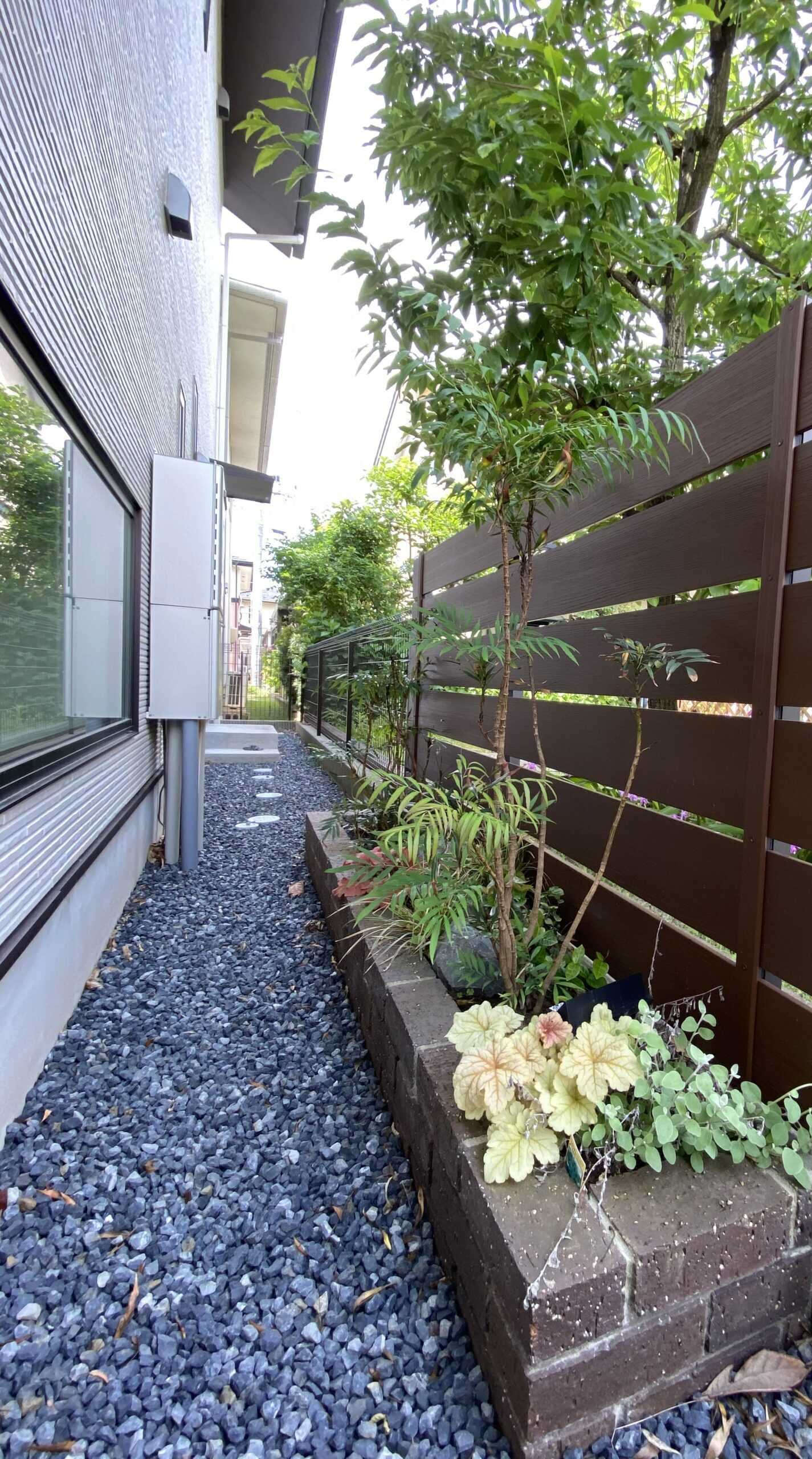 植栽で彩られたレンガ調の植え込みスペースと、ブラウンの横板フェンスが設置された建物の側面通路